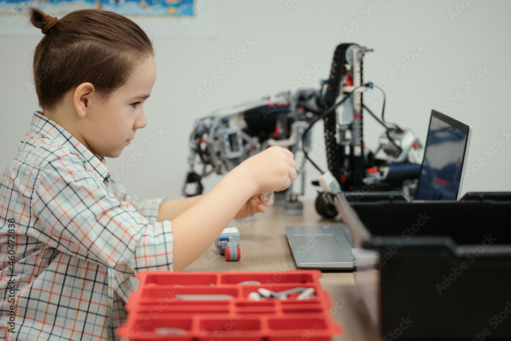Boy using a laptop to program assembled robot from plastic bricks. STEM Education for kids. Boy using a laptop to program assembled robot from plastic bricks. STEM Education for kids.