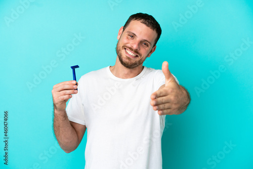 Brazilian man shaving his beard isolated on blue background shaking hands for closing a good deal