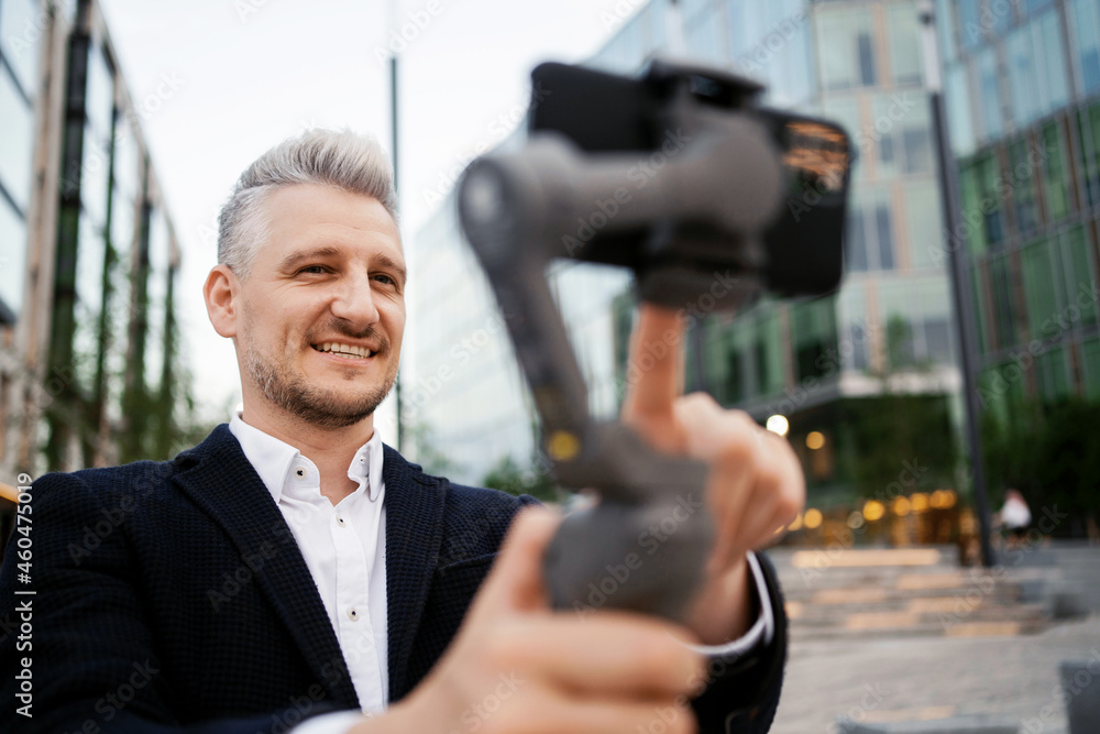 Manager Gray uses a stabilizer for video shooting on the street near the office in the city center. An economist in a business suit and with pleasure. Manager Gray uses a stabilizer for video shooting on the street near the office in the city center. An economist in a business suit and with pleasure.