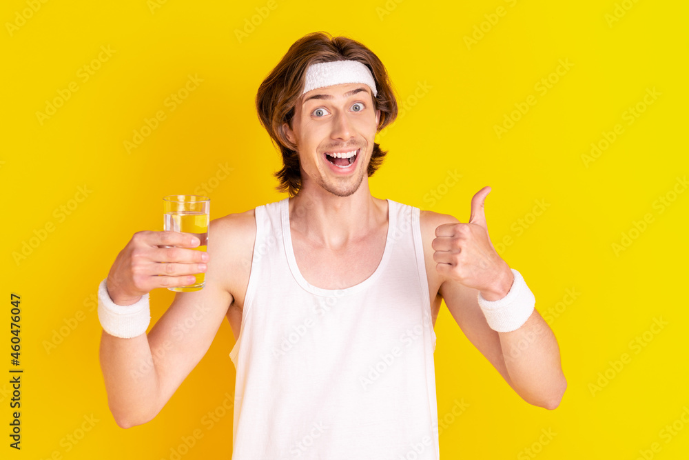 Portrait of attractive cheerful guy drinking water showing thumbup isolated over vivid yellow color background Portrait of attractive cheerful guy drinking water showing thumbup isolated over vivid yellow color background