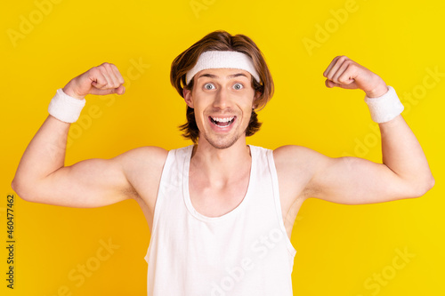 Portrait of attractive cheerful strong guy demonstrating muscles isolated over bright yellow color background © deagreez