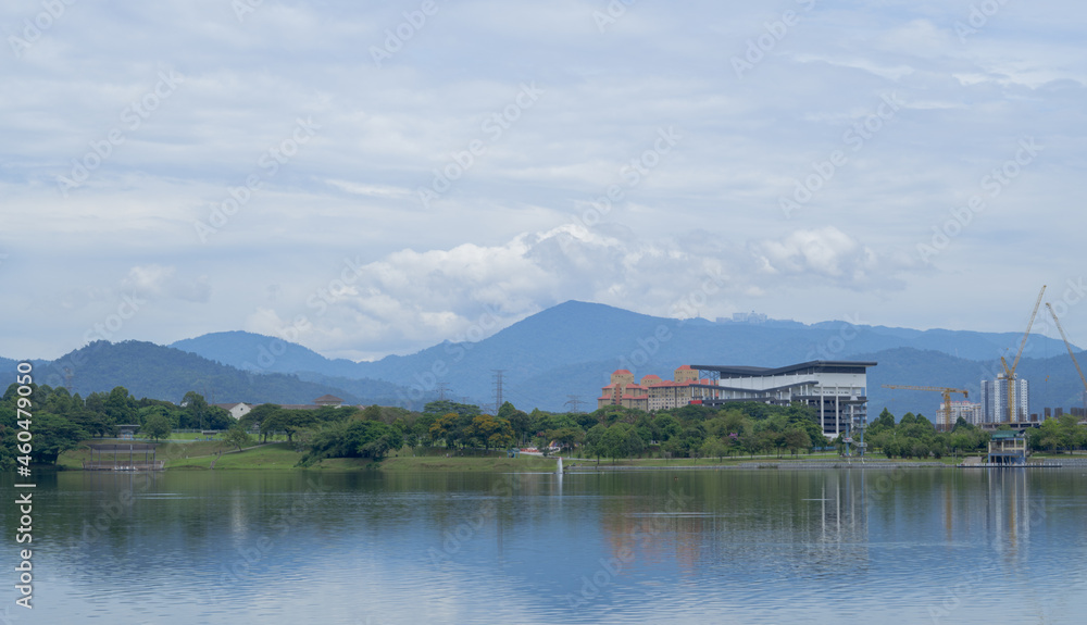 Landscape of Kepong lake in Kuala Lumpur during sunny day with reflection on water, clouds and mountains in the background. 