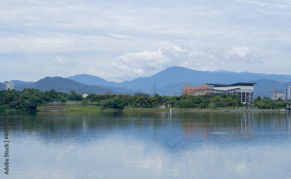 Landscape of Kepong lake in Kuala Lumpur during sunny day with reflection on water, clouds and mountains in the background. 