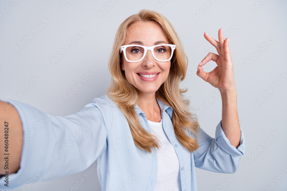 Portrait of young pretty smiling female in spectacles take selfie showing okay sign isolated on grey color background Portrait of young pretty smiling female in spectacles take selfie showing okay sign isolated on grey color background