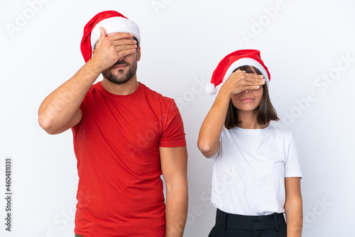 Young couple with christmas hat isolated on white background covering eyes by hands. Do not want to see something