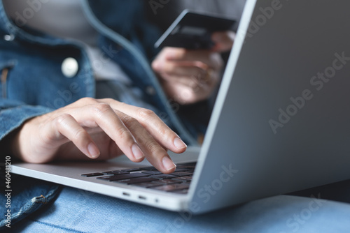 Young woman sitting on sofa at home, hand holding credit card and using laptop computer for internet payment, digital banking and online shopping, E-commerce concept