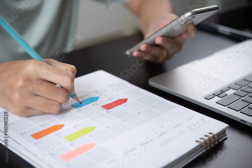 Event planner timetable agenda plan on year 2022 schedule event. Business woman checking planner on mobile phone, taking note on calendar desk on office table photo