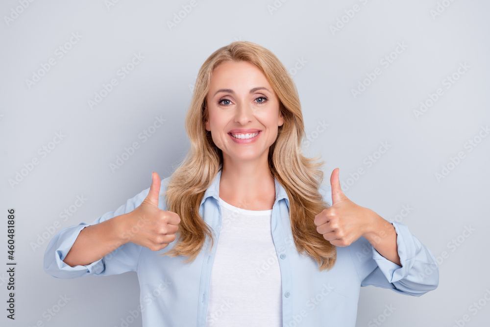 Photo of positive nice lady raise two thumbs up agree toothy smile wear blue shirt isolated grey color background Photo of positive nice lady raise two thumbs up agree toothy smile wear blue shirt isolated grey color background