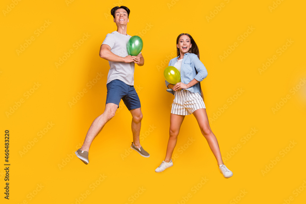 Full length body size view of nice trendy cheerful couple jumping holding balls isolated over bright yellow color background