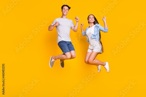 Full length body size view of nice trendy cheerful couple jumping having fun isolated over bright yellow color background