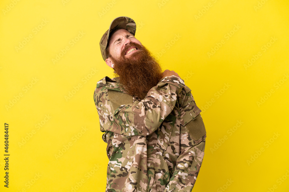 Military Redhead man over isolated on yellow background suffering from pain in shoulder for having made an effort