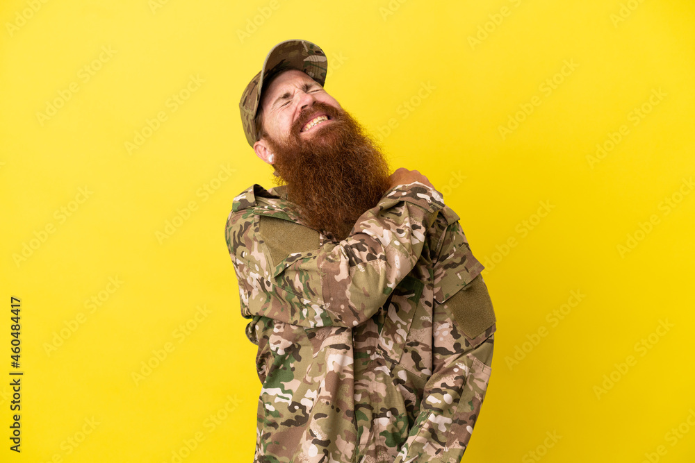 Military Redhead man over isolated on yellow background suffering from pain in shoulder for having made an effort Military Redhead man over isolated on yellow background suffering from pain in shoulder for having made an effort