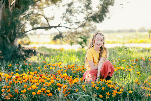 Portrait of pretty girl sitting in field with vibrant gazania wildflowers