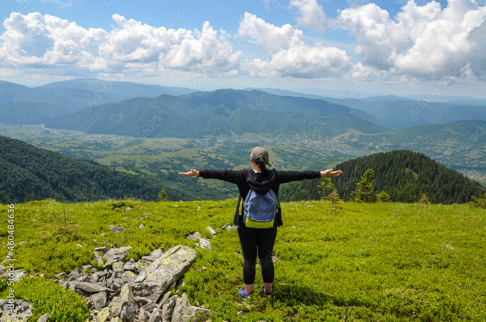 Tourist girl hiker with backpack raised arm hands and looking to valley and enjoying this view in Carpathian Mountains, Ukraine