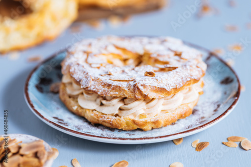Dessert called Paris Brest on a grey background with powder sugar and almond leaves and almond creme between