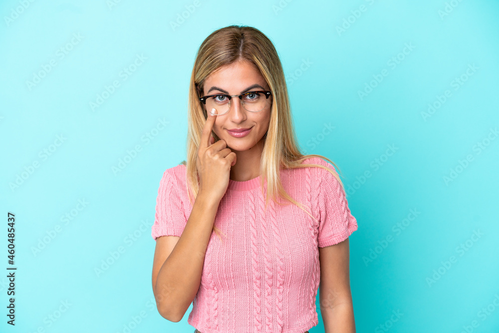 Blonde Uruguayan girl isolated on blue background showing something Blonde Uruguayan girl isolated on blue background showing something