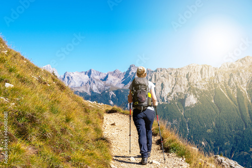 Woman hiking a trail in the Italian alps at the end of summer or fall. Dolomite peaks of Rosengarten - Catinaccio are visible in the background. Carezza, Val d'Ega - Trentino, Italy