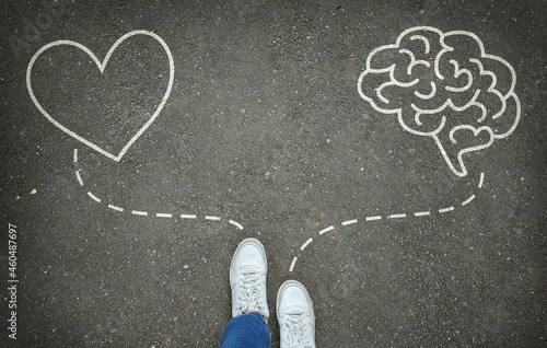 Heart or brain. Legs in white sneakers in front of white heart and brain symbols on the gray asphalt background. Path choice concept