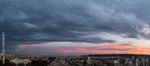 Stormy gray clouds is coming to seaside city at sunset. Panorama of dramatic overcast sky at evening. Dark stratus clouds hang over Varna. Weather change concept. Storm is coming wide landscape.  photo