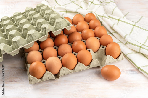 One brown chicken egg out of the full cardboard tray on a white wooden table. Fresh organic hen eggs with brown shell in the biodegradable carton container. Healthy eating protein ingredient. photo