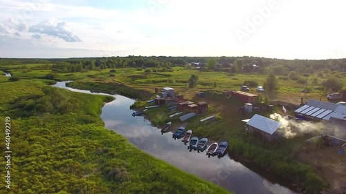 Flight over a Small River and Village.	The camera flies over a small river. There is a village on the bank of the river. There are boats near the shore. Smoke comes from the chimney of a small house.