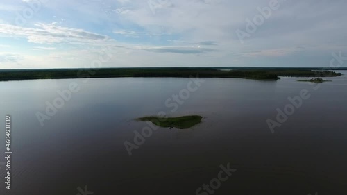 Small Island in Middle of Lake.	The camera flies low on the surface of the lake and a small island. There is reed growing on the island