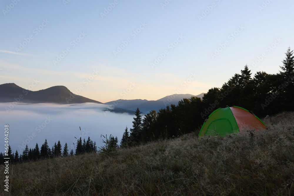 Picturesque mountain landscape with camping tent in foggy morning. Space for text