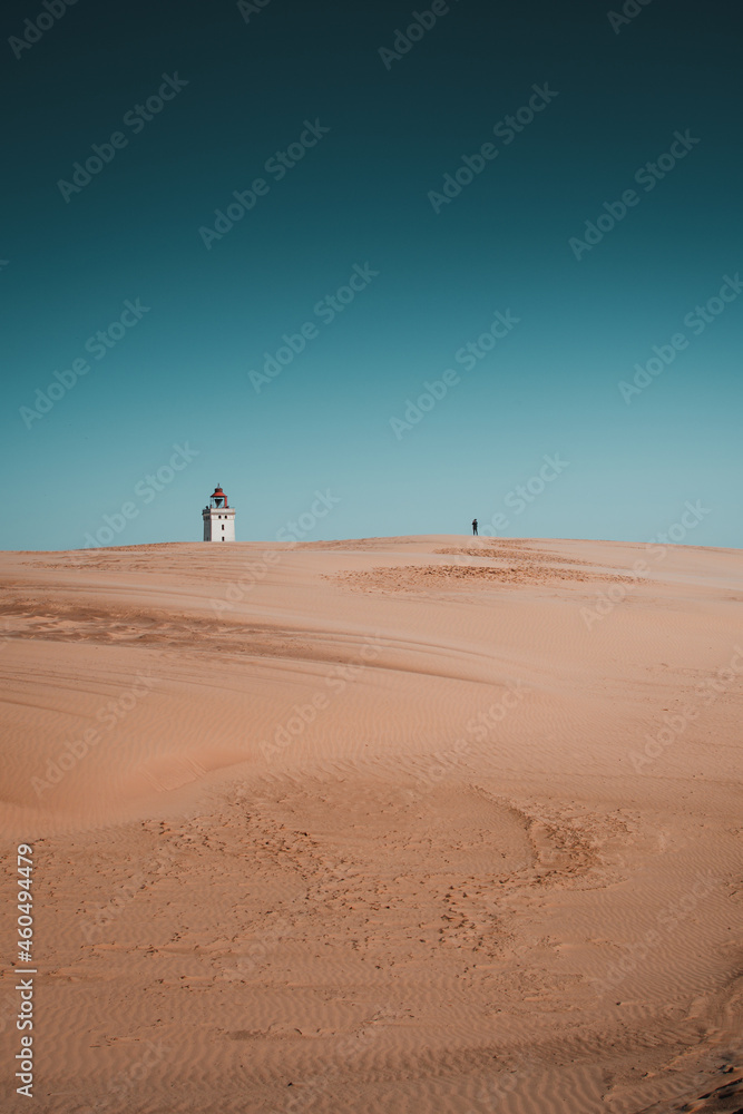 Exploring the famous ancient Rubjerg knude fyr place in the endless sand dunes. Desert like sand dunes with the landmark lighthouse on a bright summer vacation day. North Jutland, Denmark, Europe Exploring the famous ancient Rubjerg knude fyr place in the endless sand dunes. Desert like sand dunes with the landmark lighthouse on a bright summer vacation day. North Jutland, Denmark, Europe