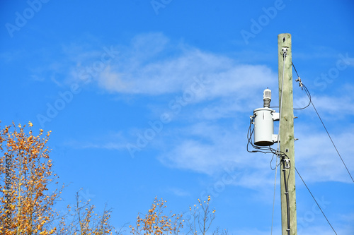 An image of a rural power transformer against a bright blue sky. 