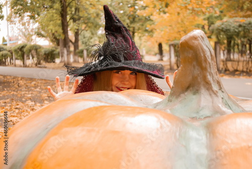 a girl who hides behind a pumpkin in a witch costume for Halloween