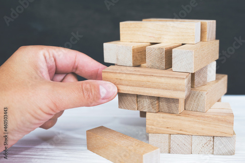 Tower made of wooden blocks and human hands take one block