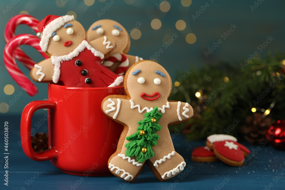 Naklejka premium Delicious homemade Christmas cookies with cup on blue wooden table against blurred festive lights