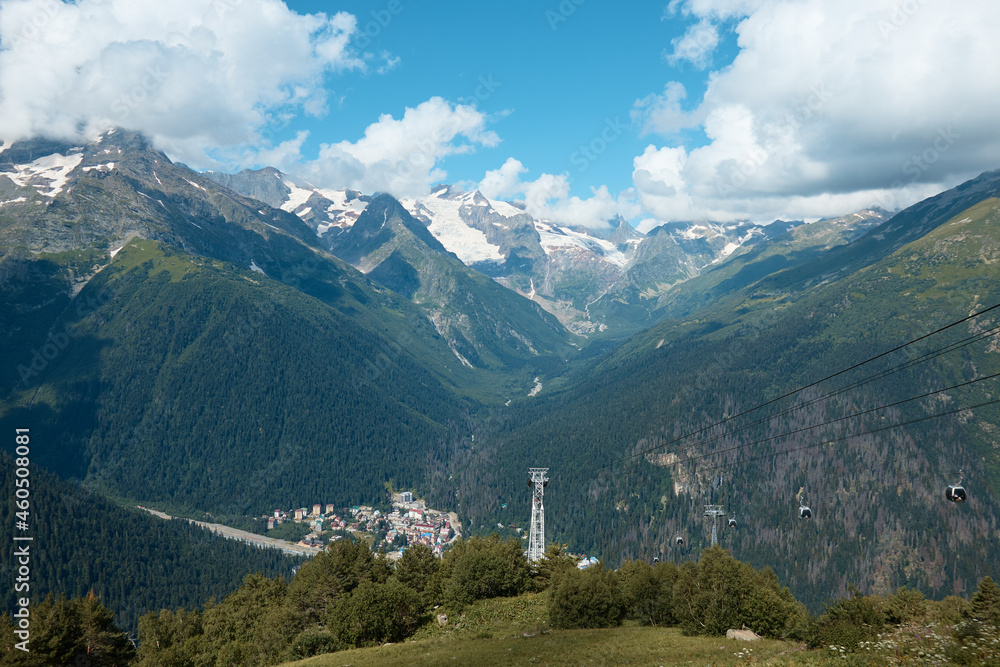 Cable car in the mountains, grass and mountains with glaciers, alpine meadows, village in the mountains