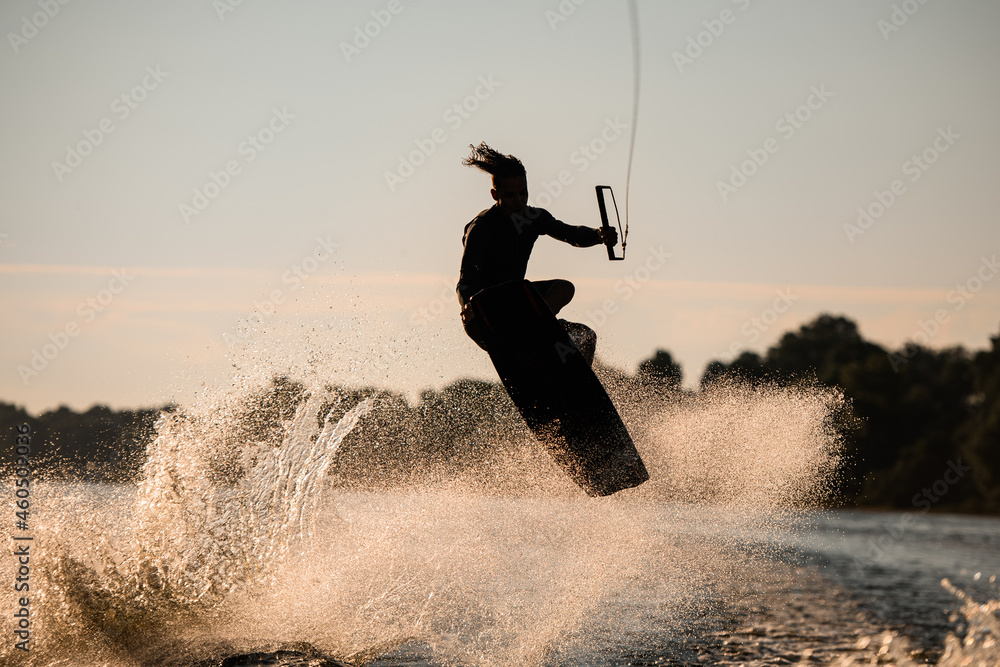 Active wakeboarder jumping with board over splashing river wave