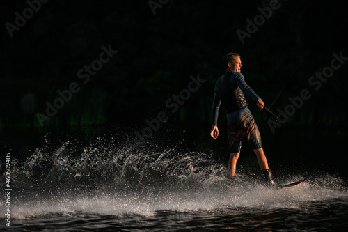 athletic man confidently rides on wakeboard at splashing river wave.
