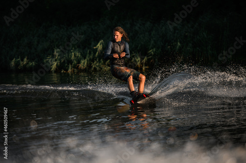 energetic man in wetsuit skillfully balancing on water surface on wakeboard