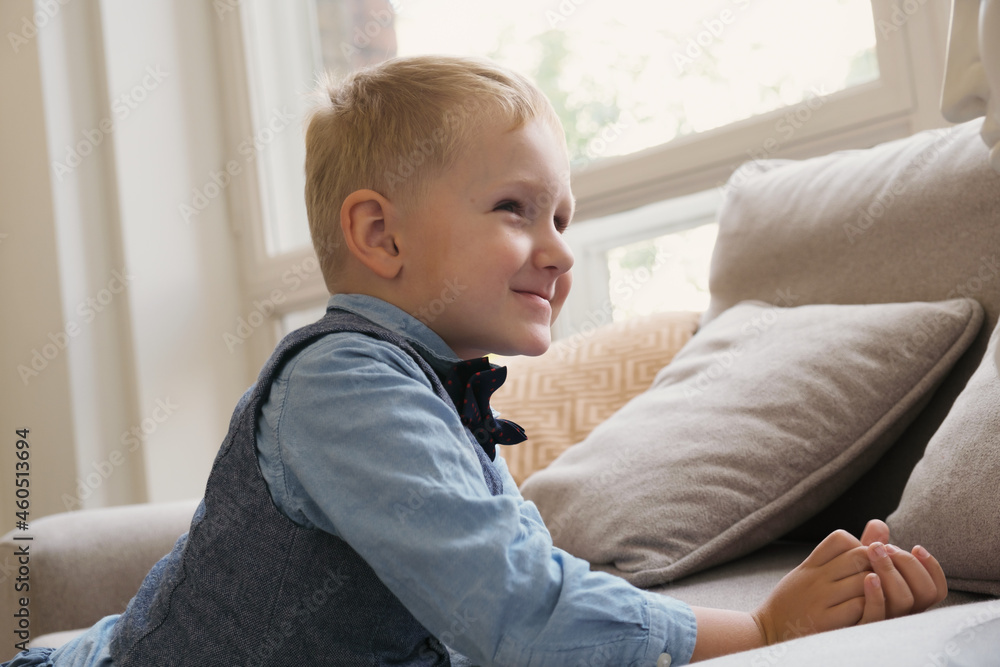 Little blonde boy folded his hands for prayer and smiled as he turned to God. A boy prays by the couch in the living room. A five-year-old cute boy dreams. Little blonde boy folded his hands for prayer and smiled as he turned to God. A boy prays by the couch in the living room. A five-year-old cute boy dreams.