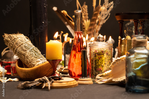Occult and esoteric witch doctor still life. Selective focus. Halloween background with magic objects. Black candles, skull, bones, and potions vials on witch table. Mystic witchery with weeds.