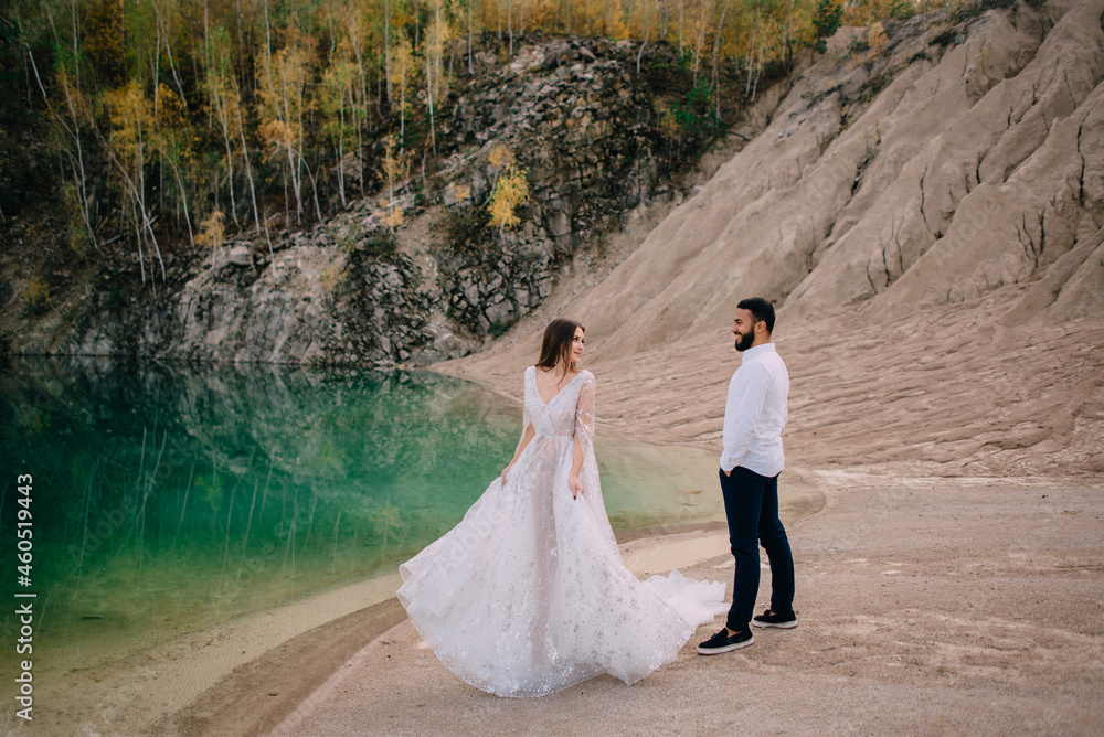 Newlyweds are standing near a beautiful lake. Middle Eastern groom and Caucasian bride embrace on the beach. Newlyweds are standing near a beautiful lake. Middle Eastern groom and Caucasian bride embrace on the beach.
