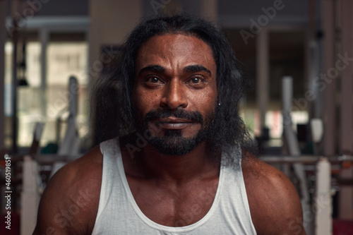 portrait of an interesting male athlete with long hair, who stands in the gym and looks directly into the camera. High quality photo