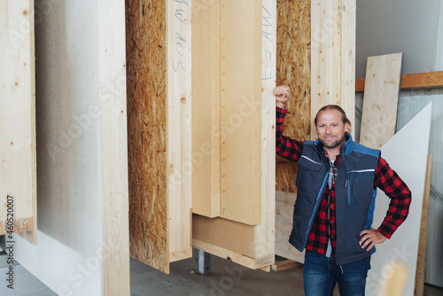 Smiling carpenter leaning against frames of prefabricated walls photo