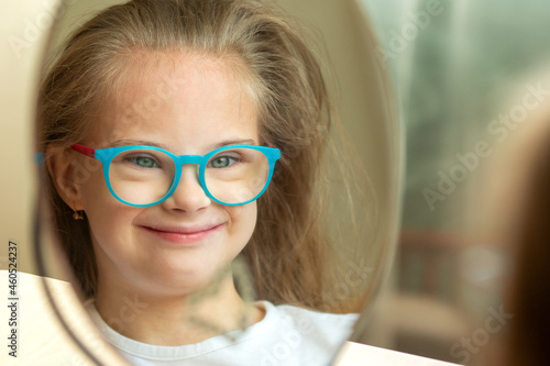 A beautiful girl with Down syndrome combs in front of a mirror
