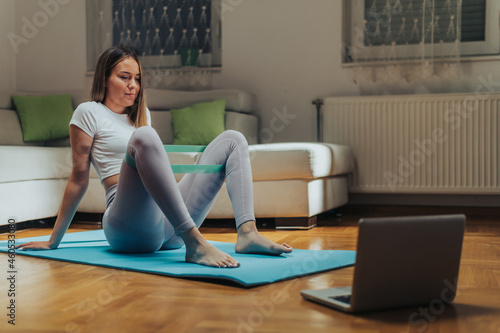 Attractive young woman using laptop while training at home