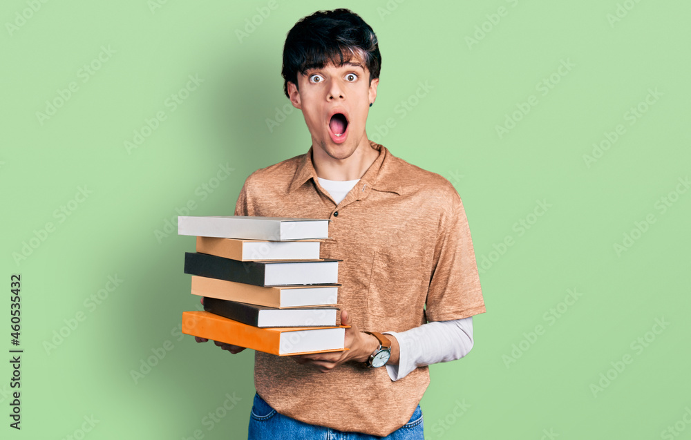 Handsome hipster young man holding a pile of books afraid and shocked with surprise and amazed expression, fear and excited face. Handsome hipster young man holding a pile of books afraid and shocked with surprise and amazed expression, fear and excited face.