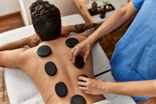 Man reciving back massage with black stones at beauty center. photo