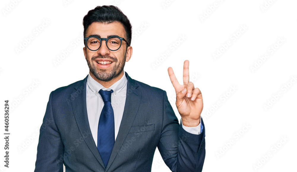 Hispanic man with beard wearing business suit and tie smiling with happy face winking at the camera doing victory sign. number two. Hispanic man with beard wearing business suit and tie smiling with happy face winking at the camera doing victory sign. number two.