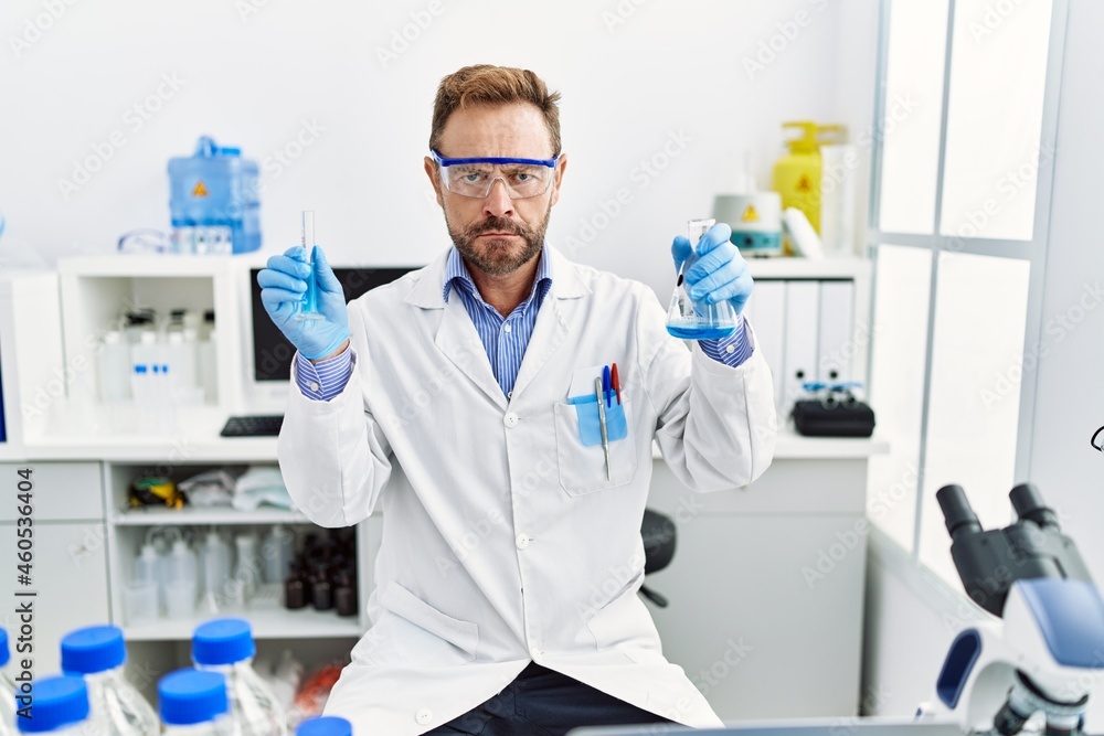 Middle age man working at scientist laboratory holding chemical products skeptic and nervous, frowning upset because of problem. negative person. Middle age man working at scientist laboratory holding chemical products skeptic and nervous, frowning upset because of problem. negative person.