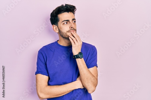 Young hispanic man wearing casual t shirt with hand on chin thinking about question, pensive expression. smiling with thoughtful face. doubt concept.