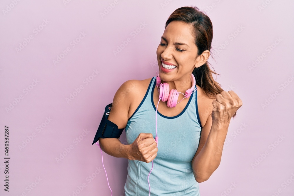 Young latin woman wearing gym clothes and using headphones celebrating surprised and amazed for success with arms raised and eyes closed Young latin woman wearing gym clothes and using headphones celebrating surprised and amazed for success with arms raised and eyes closed