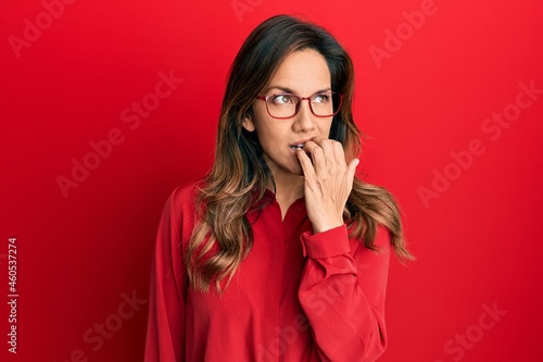 Young latin woman wearing casual clothes and glasses looking stressed and nervous with hands on mouth biting nails. anxiety problem. © Krakenimages.com